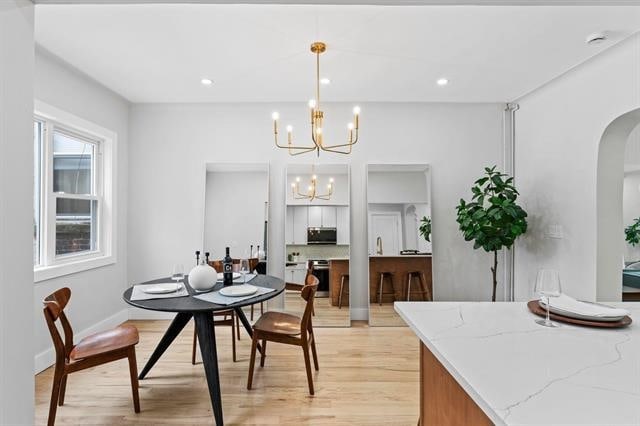 dining room featuring arched walkways, recessed lighting, light wood-style flooring, and a notable chandelier