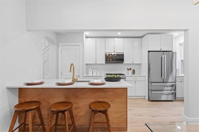 kitchen featuring decorative backsplash, appliances with stainless steel finishes, a breakfast bar, light countertops, and white cabinetry