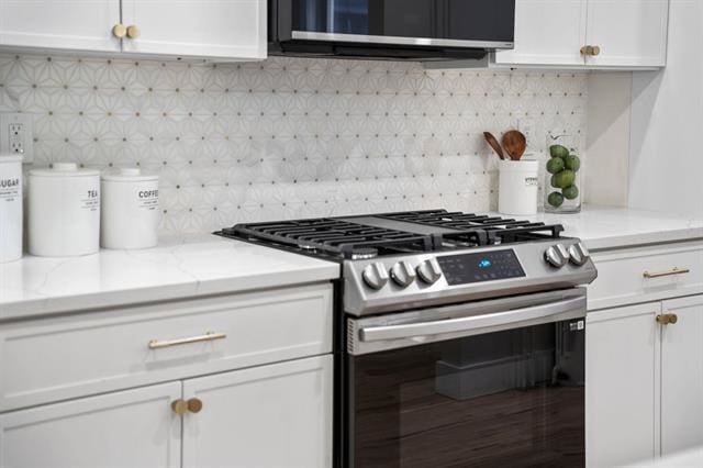 kitchen featuring appliances with stainless steel finishes, white cabinetry, backsplash, and light stone countertops