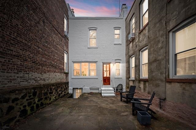 back of property at dusk with entry steps, brick siding, a chimney, and a patio area