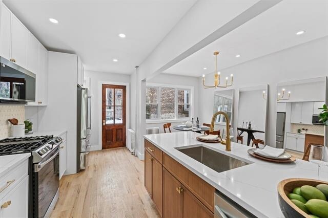 kitchen with stainless steel appliances, light wood-style floors, a sink, and backsplash