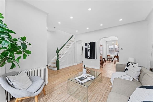 living room featuring arched walkways, light wood-style flooring, recessed lighting, stairs, and radiator