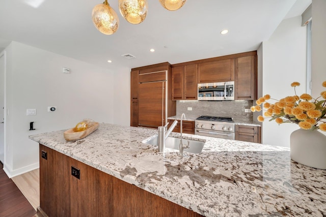 kitchen with light stone counters, wood finished floors, a sink, appliances with stainless steel finishes, and backsplash