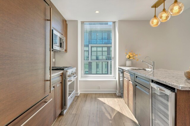 kitchen with baseboards, beverage cooler, light wood-style flooring, stainless steel appliances, and a sink