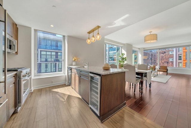 kitchen with pendant lighting, beverage cooler, light stone counters, wood finished floors, and stainless steel appliances