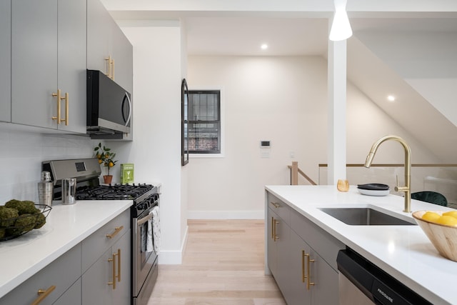 kitchen featuring pendant lighting, sink, gray cabinetry, stainless steel appliances, and light hardwood / wood-style floors