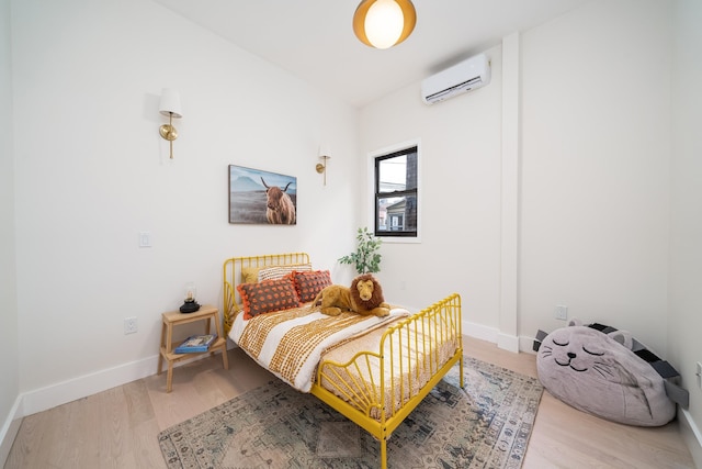 bedroom featuring an AC wall unit, light wood-style flooring, and baseboards