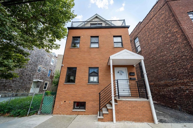 view of front of home featuring a balcony, brick siding, fence, and a gate