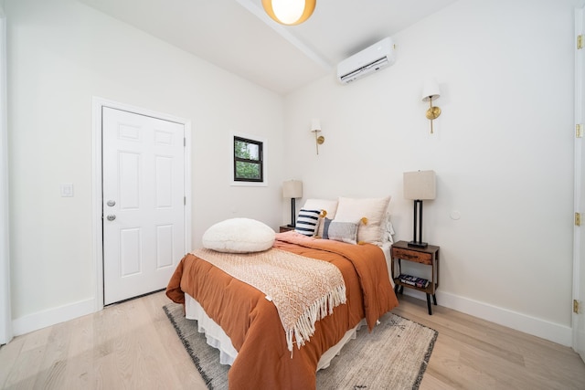 bedroom featuring light wood-type flooring, baseboards, and a wall mounted AC