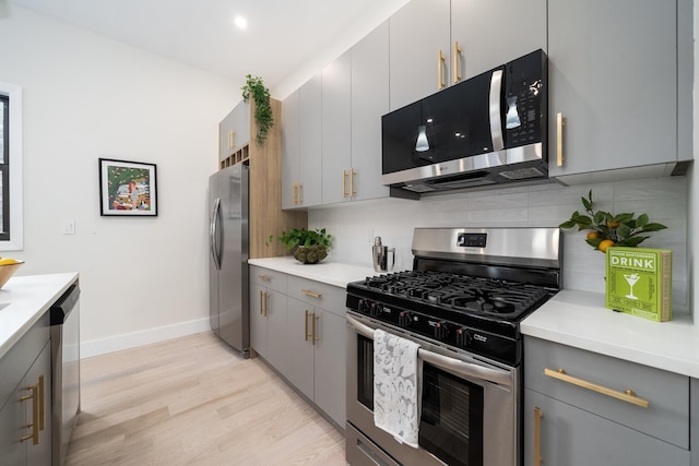 kitchen featuring light wood finished floors, decorative backsplash, appliances with stainless steel finishes, gray cabinets, and light countertops