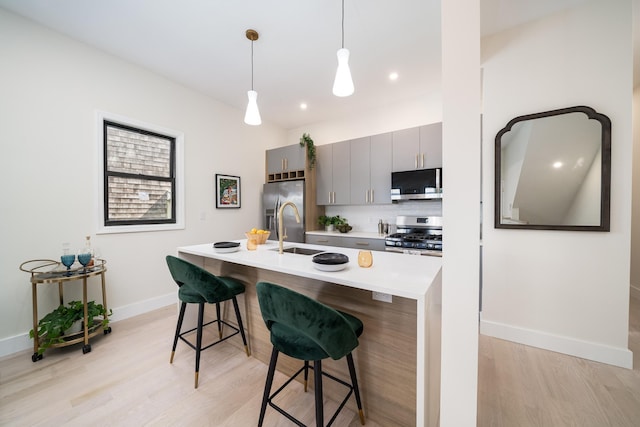 kitchen featuring appliances with stainless steel finishes, a breakfast bar area, a kitchen island with sink, gray cabinetry, and light wood-type flooring