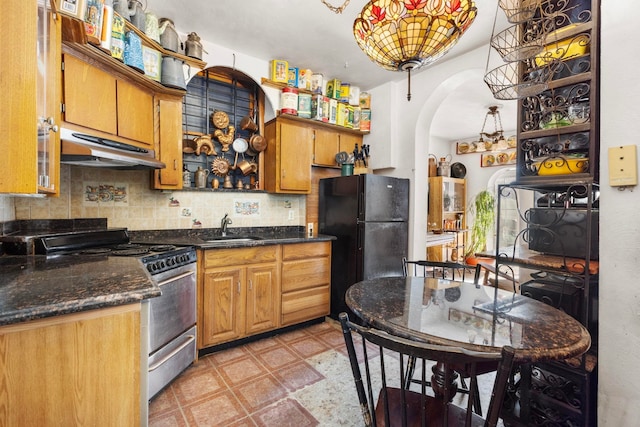 kitchen featuring sink, stainless steel gas range, dark stone countertops, backsplash, and black fridge