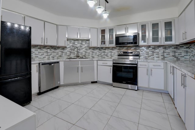 kitchen featuring appliances with stainless steel finishes, a sink, white cabinetry, decorative backsplash, and glass insert cabinets