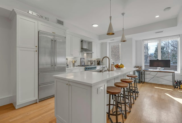 157 8th St, Hoboken, NJ 07030 - kitchen featuring built in fridge, wall chimney exhaust hood, light wood-style floors, a kitchen island with sink, and light countertops