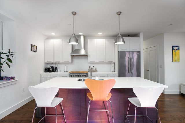 kitchen with decorative light fixtures, a kitchen island with sink, appliances with stainless steel finishes, and wall chimney range hood