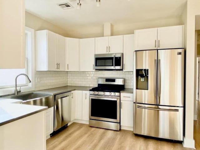 kitchen with appliances with stainless steel finishes, white cabinets, visible vents, decorative backsplash, and a sink