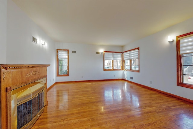 unfurnished living room featuring a glass covered fireplace, light wood-style flooring, baseboards, and visible vents