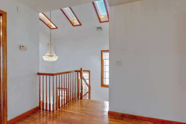 corridor featuring wood finished floors, visible vents, baseboards, vaulted ceiling with skylight, and an upstairs landing