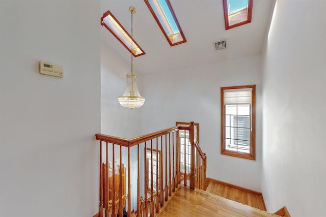 stairs featuring wood finished floors, visible vents, baseboards, an inviting chandelier, and lofted ceiling with skylight