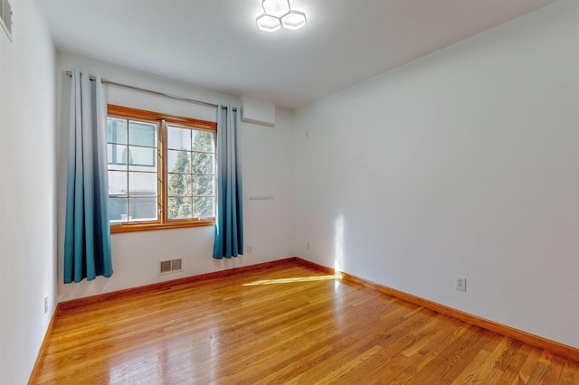 spare room featuring wood finished floors, visible vents, and baseboards