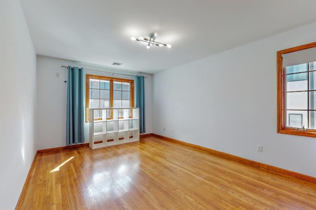 empty room with light wood-type flooring, baseboards, a healthy amount of sunlight, and visible vents