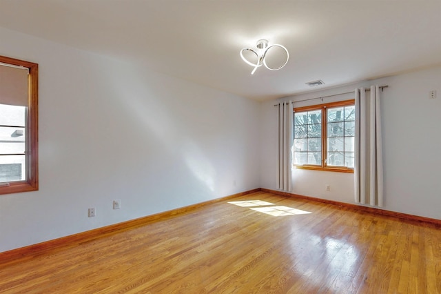 empty room featuring light wood finished floors, visible vents, and baseboards