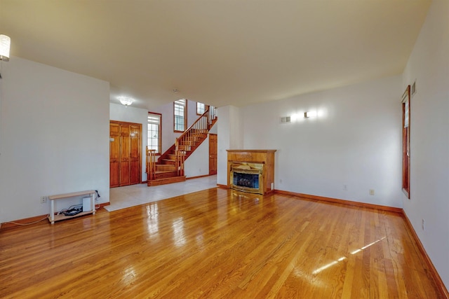 unfurnished living room with visible vents, baseboards, a fireplace, stairs, and light wood-type flooring