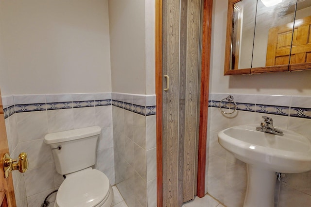 bathroom featuring tile patterned floors, a wainscoted wall, toilet, and tile walls