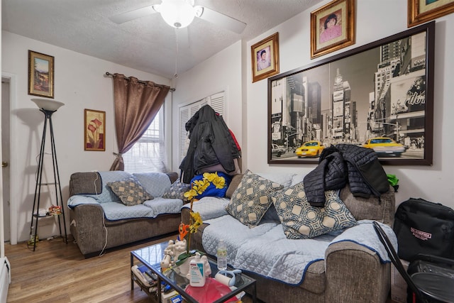 living room with ceiling fan, wood-type flooring, a textured ceiling, and a baseboard heating unit