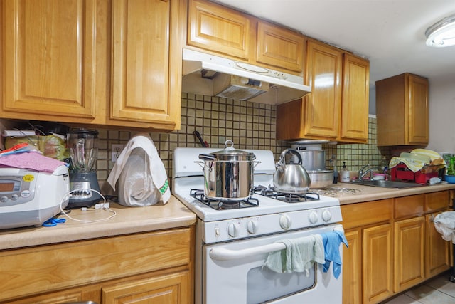 kitchen with tasteful backsplash, sink, light tile patterned flooring, and white gas range oven