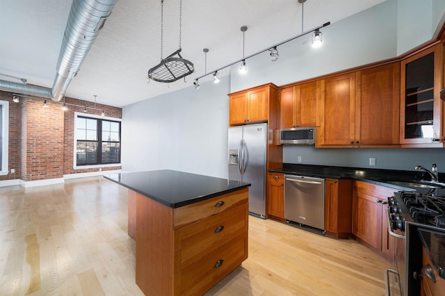 kitchen featuring a kitchen island, brick wall, appliances with stainless steel finishes, sink, and hanging light fixtures