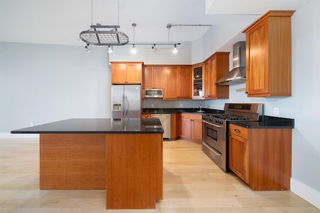 kitchen with pendant lighting, appliances with stainless steel finishes, a kitchen island, wall chimney exhaust hood, and light wood-type flooring