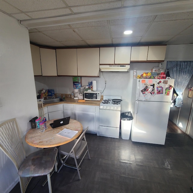 kitchen with white appliances, a drop ceiling, light countertops, under cabinet range hood, and a sink