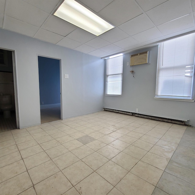 empty room featuring a wall unit AC, light tile patterned floors, a baseboard heating unit, and a drop ceiling