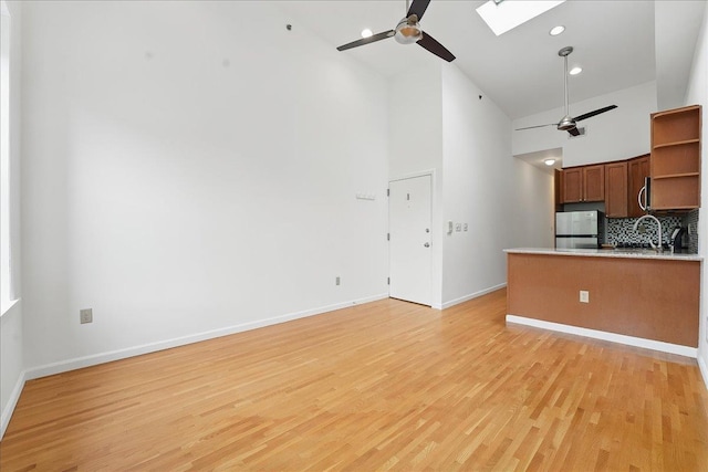 kitchen featuring high vaulted ceiling, ceiling fan, appliances with stainless steel finishes, a skylight, and backsplash