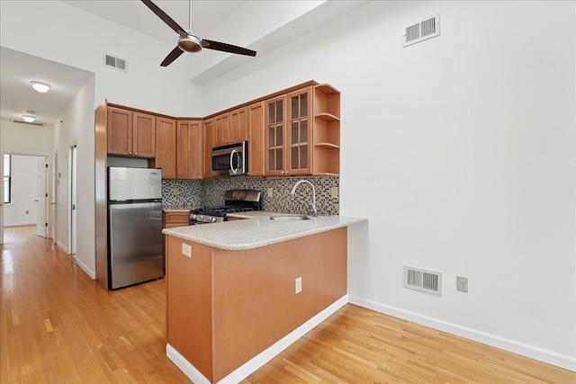 kitchen with stainless steel appliances, a sink, brown cabinetry, light wood finished floors, and a high ceiling