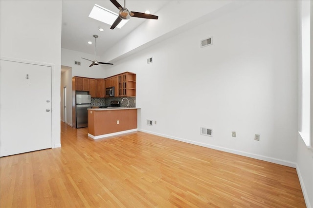 kitchen featuring ceiling fan, open shelves, stainless steel appliances, a high ceiling, and a skylight