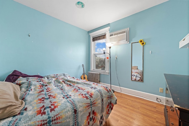 bedroom featuring radiator, an AC wall unit, baseboards, and wood finished floors