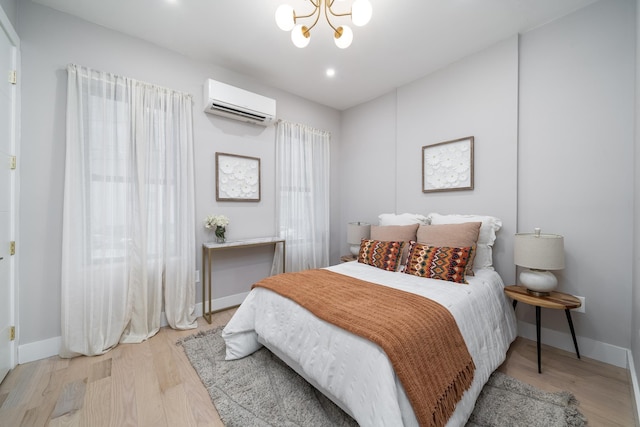 bedroom featuring a chandelier, light wood-style flooring, baseboards, and a wall mounted AC