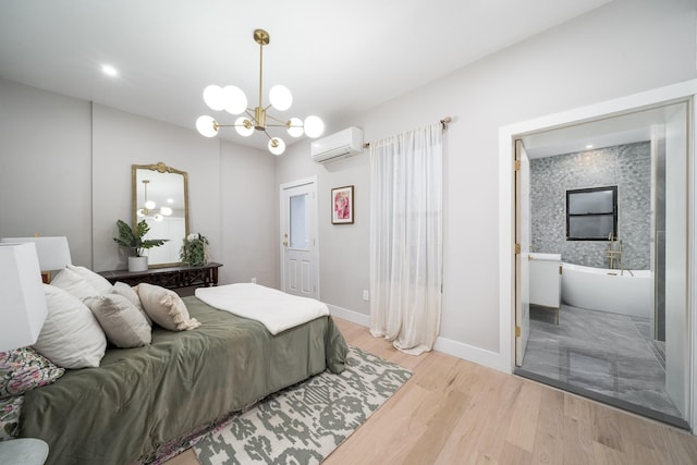 bedroom featuring a wall unit AC, connected bathroom, baseboards, light wood finished floors, and an inviting chandelier