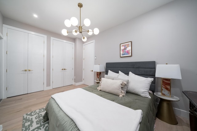 bedroom featuring baseboards, light wood-style flooring, an inviting chandelier, and two closets