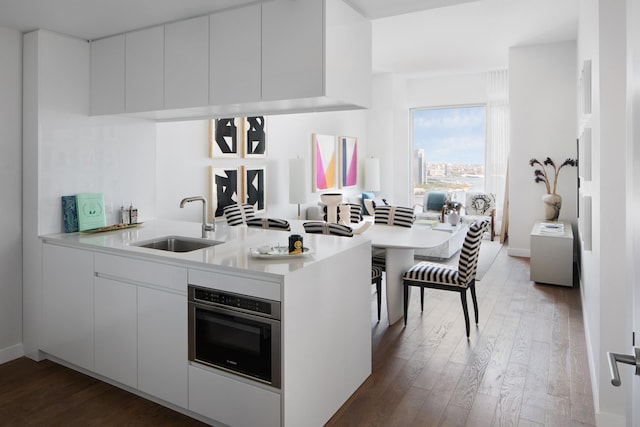 kitchen with kitchen peninsula, stainless steel oven, dark wood-type flooring, sink, and white cabinetry