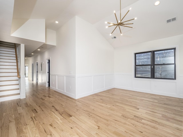 empty room featuring an inviting chandelier, vaulted ceiling, and light wood-type flooring