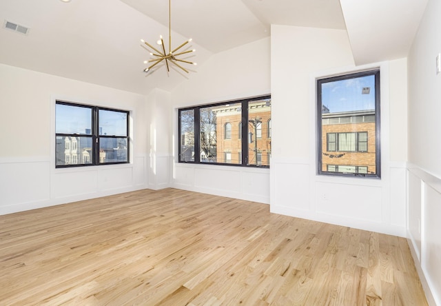 spare room featuring light wood-type flooring, vaulted ceiling, and an inviting chandelier