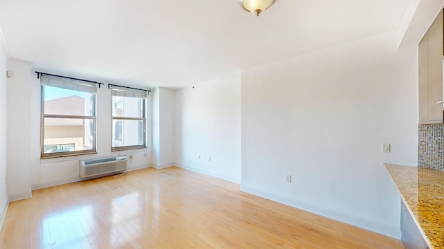 unfurnished room featuring light wood-style floors, baseboards, and a wall unit AC