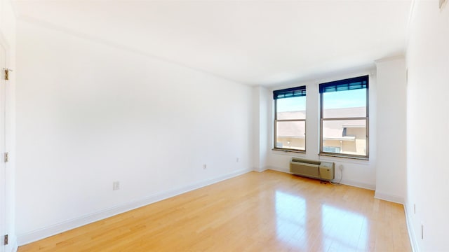 unfurnished room with light wood-style floors, baseboards, and an AC wall unit