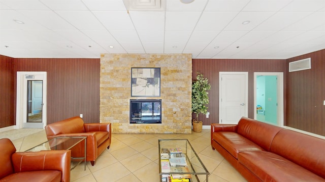 living area with light tile patterned flooring, baseboards, a drop ceiling, and a fireplace