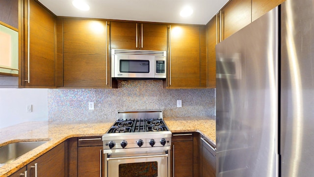 kitchen featuring light stone counters, backsplash, brown cabinets, and stainless steel appliances