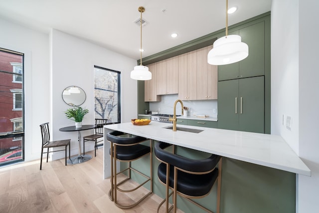 kitchen with pendant lighting, a kitchen bar, light wood-type flooring, decorative backsplash, and a sink