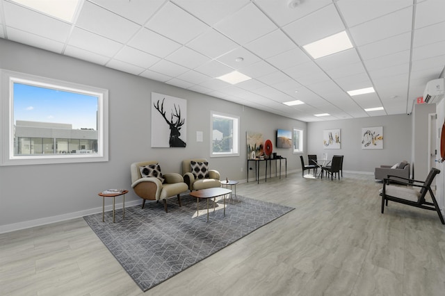 sitting room with a drop ceiling, an AC wall unit, baseboards, and light wood-style floors